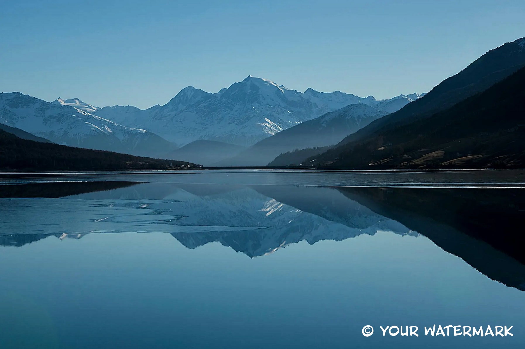 Snow-capped mountains reflected in a calm lake with a single-line text copyright-style watermark in a corner